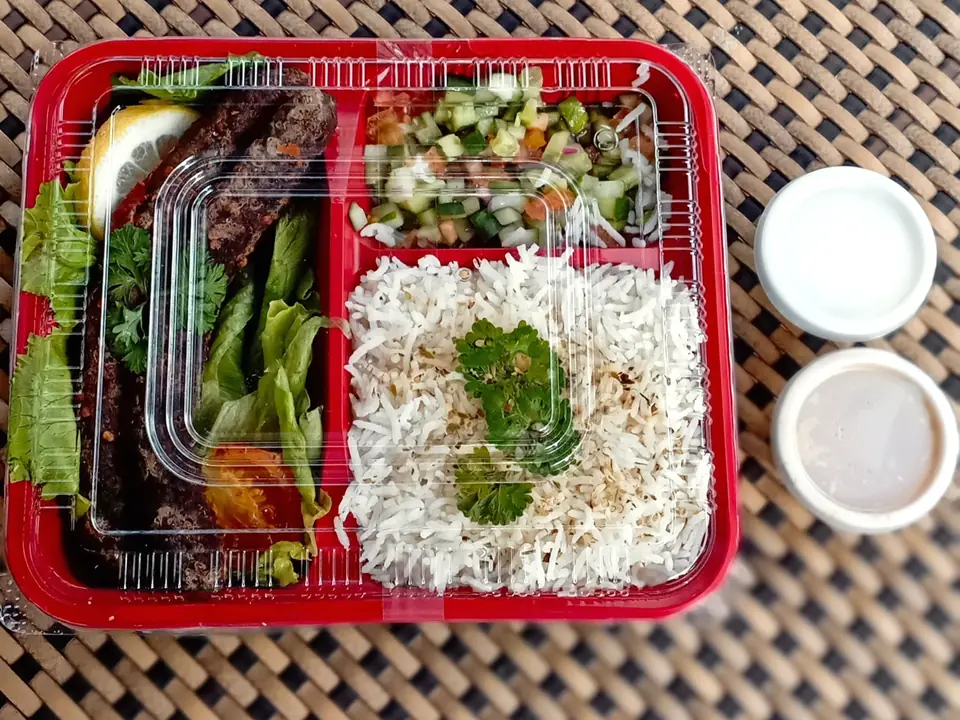 A Sababa platter of rice, salad and sauces in a red tray